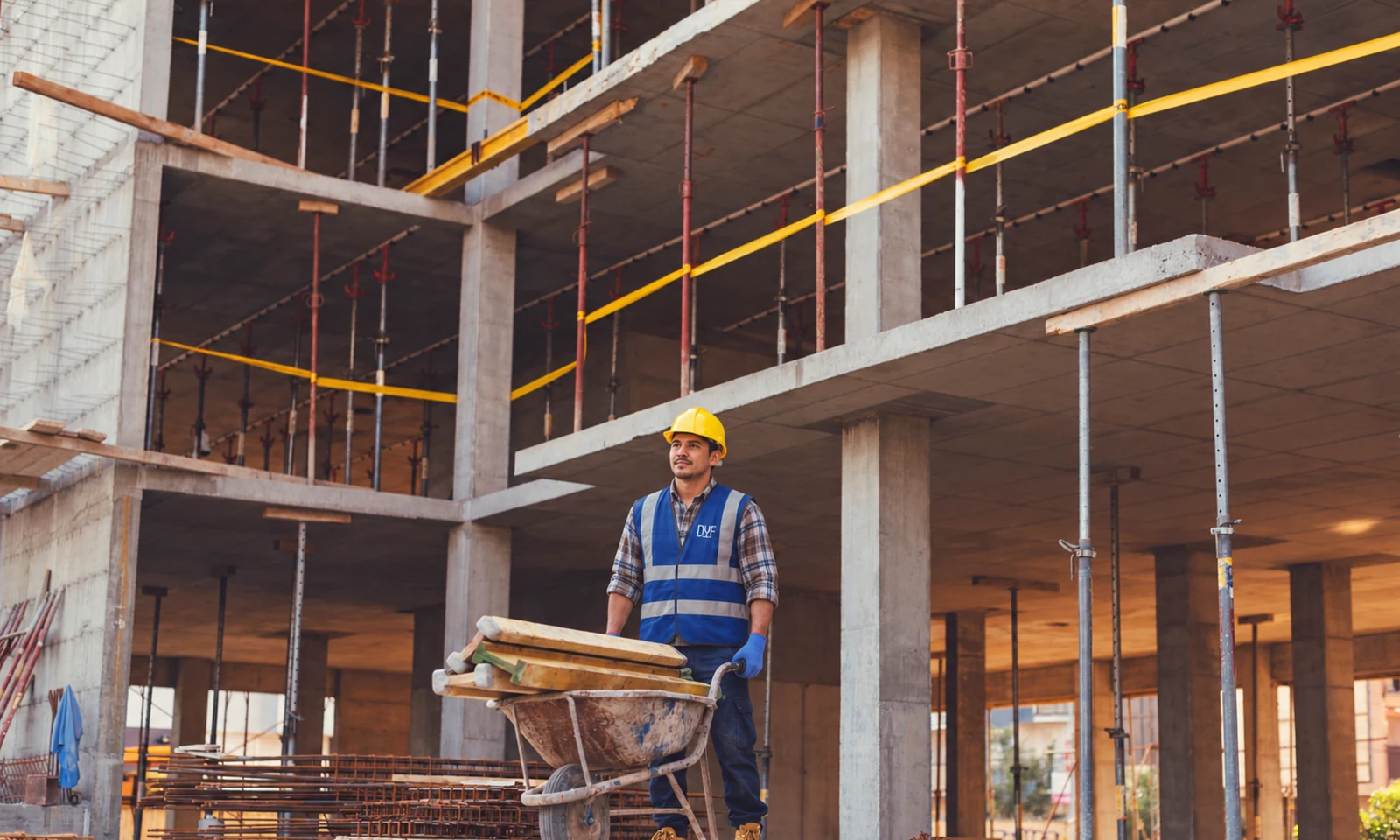 Trabajador DyF con casco amarillo y una carretilla en una estructura de concreto en construcción.